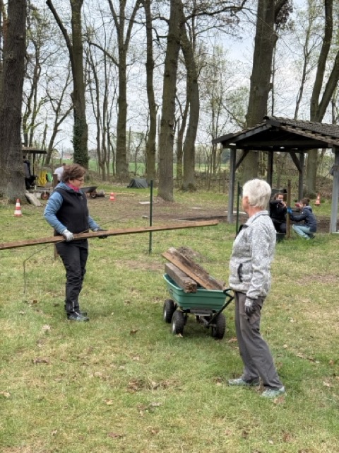 Zwei Helfer transportieren Holzbalken über den Platz während des Arbeitseinsatzes 2026.