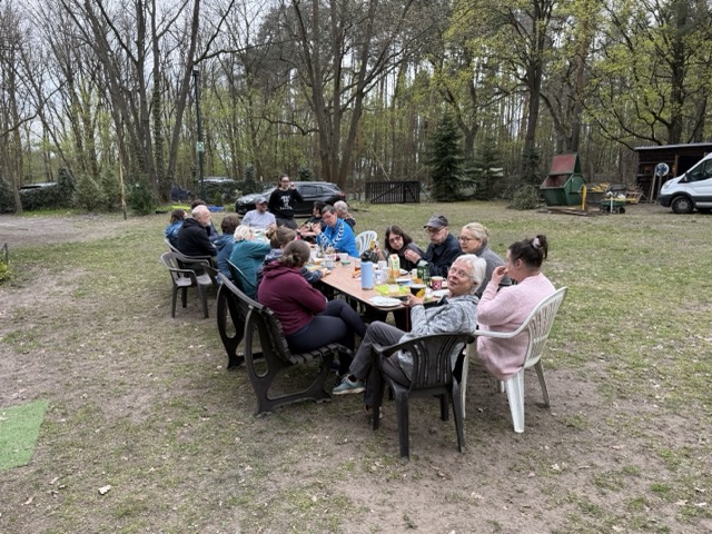 Mitglieder sitzen nach getaner Arbeit gemeinsam am Frühstückstisch auf dem Platz.